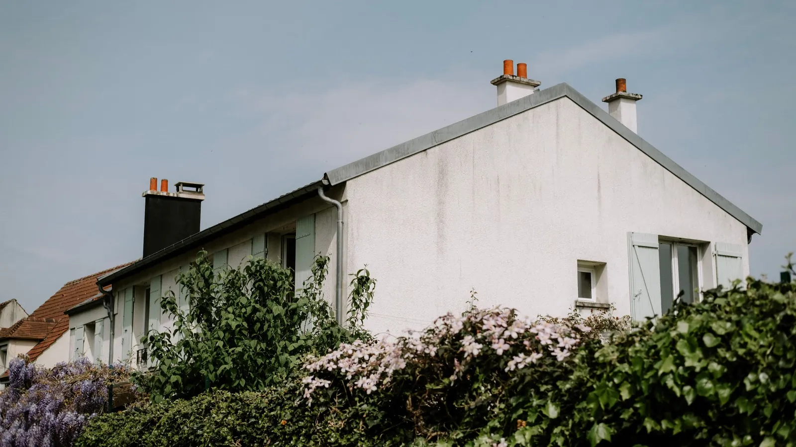 Pavillon enduit blanc au toit de tuiles, derrière des lilas en fleurs
