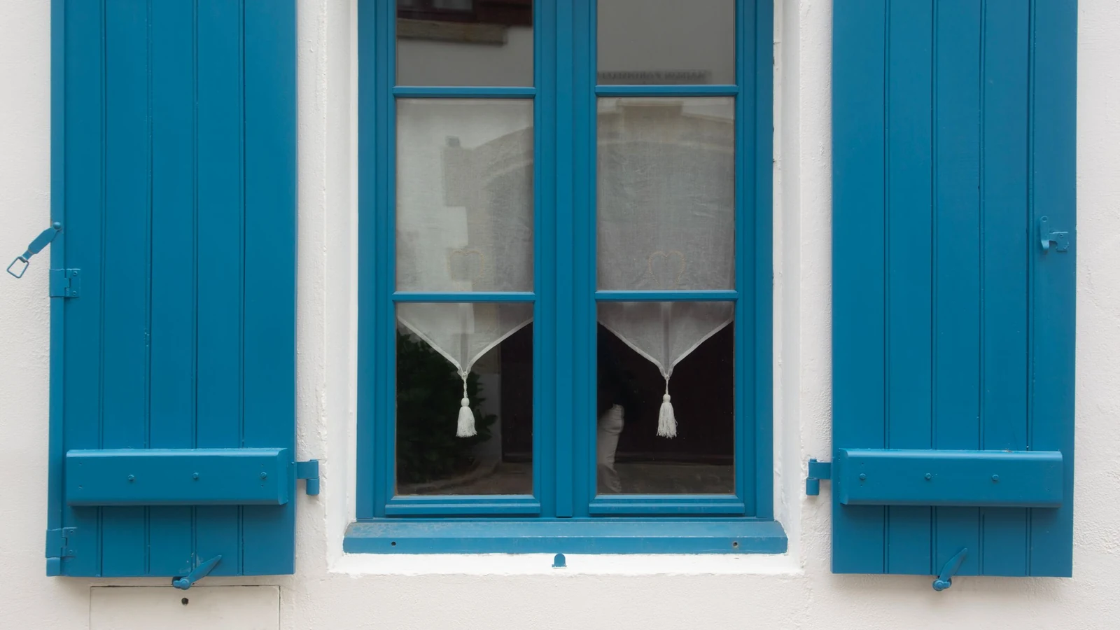 Volets en bois peints en bleu de part et d'autre d'une fenêtre